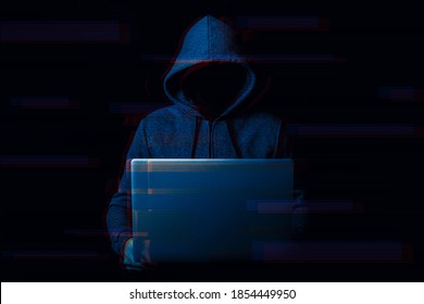 Man without a face in a hood holds a laptop in his hands on a dark background. Concept of cyber rogue, hacker. Banner. Added glitch effect - Shutterstock ID 1854449950