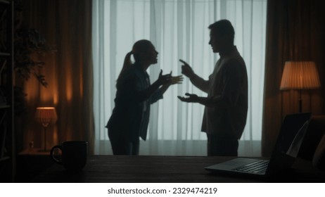 A man and a woman are arguing in the living room near the window. A silhouette of a couple arguing over the fact that the man spends too much time on the laptop. - Powered by Shutterstock