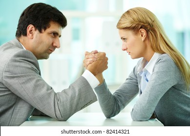 Man and woman in arm wrestling gesture on working table during meeting