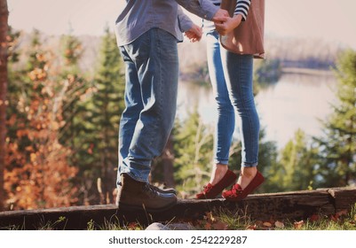 Man and woman balancing on a wooden beam in a fall scene by a lake.  Holding hands. Fall fashion - Powered by Shutterstock