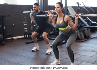 Man and woman with barbell flexing muscles in gym