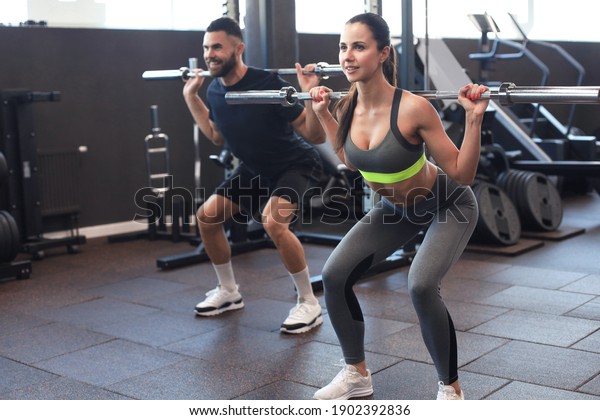 Man and\
woman with barbell flexing muscles in\
gym
