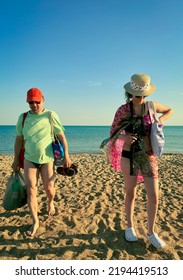 A Man And A Woman With Beach Bags Leave The Beach. Time To Leave The Evening Beach. End Of Summer Vacation Concept