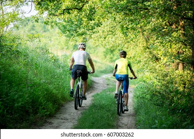 Man and woman are bicycles. Cyclists man and a woman with bicycles go near the fields at sunset in summer. - Powered by Shutterstock