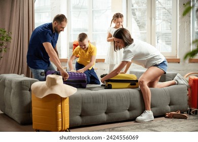 Man, woman, boy and girl sorting garments for travel, nd packaging bags in bright living room. Joyful mood before trip. Family resort. Concept of tourism, holiday, vacation, relaxation. Ad