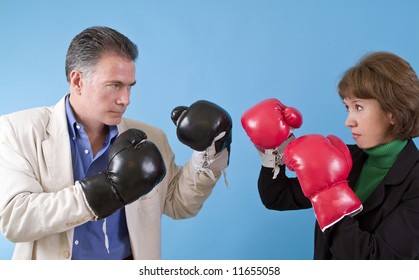 A man and a woman in business suits wearing boxing gloves as if ready to fight.
