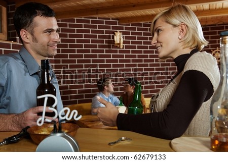 Man and woman chatting in bar, smiling at each other, young couple in background.?