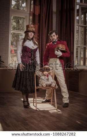 A man, a woman and a child, dressed in steampunk style clothes, posing in the interior against the background of large windows and screens