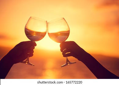Man and woman clanging wine glasses with champagne at sunset dramatic sky background