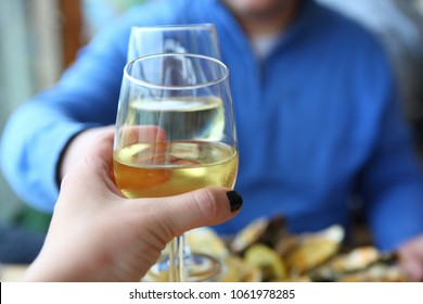 Man and woman clink glasses during romantic dinner in the restaurant in Yerseke on oyster farm in the Netherlands. Hands with glass of white chardonnay wine, oyster mollusks