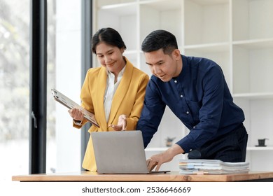 A man and woman collaborate at a workspace, reviewing documents on a laptop, embodying teamwork and professional engagement. - Powered by Shutterstock