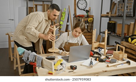 Man and woman collaborating in a well-equipped carpentry workshop, focusing on a craft project and laptop. - Powered by Shutterstock