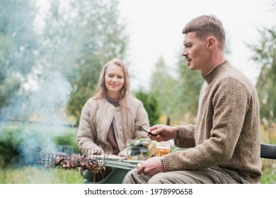 A Man And A Woman Cook A Barbecue Together In Nature. In A Dacha Village On Its Own Plot Of Land. Warm Autumn Weather, Cozy Family Dinner.