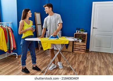 Man And Woman Couple Drinking Coffee Ironing Clothes At Laundry Room