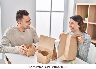 Man And Woman Couple Eating Take Away Food Sitting On Table At Home