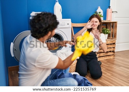 Man and woman couple smiling confident playing with cleaning clothes at laundry room