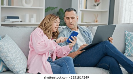 Man and woman couple using laptop and smartphone sitting on sofa at home - Powered by Shutterstock