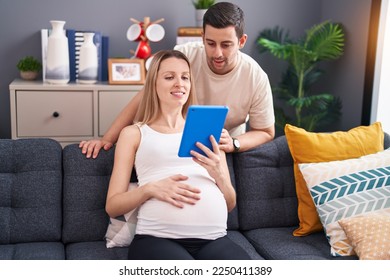 Man and woman couple using touchpad expecting baby at home - Powered by Shutterstock