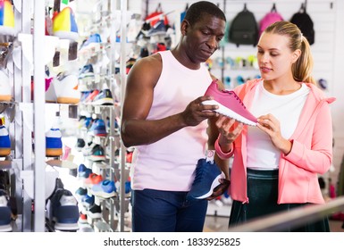 Man And Woman Customers Choosing Sports Shoes In Sporting Goods Shop