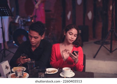 A man and a woman dating in a fancy restaurant ignore each other and use their cellphones as they are both uninterested in their first date. Checking each other's phone. Couples with trust issues. - Shutterstock ID 2260403513