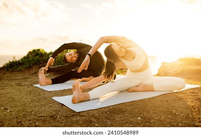 Man and woman deeply engaged in yoga, stretching on mats with the glowing sunset behind them, highlighting their serene coastal fitness routine - Powered by Shutterstock