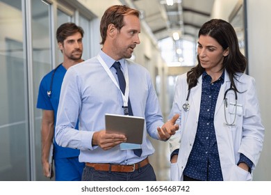 Man and woman doctor having a discussion in hospital hallway. Doctor discussing patient case status with his medical staff after operation. Pharmaceutical representative showing medical report.