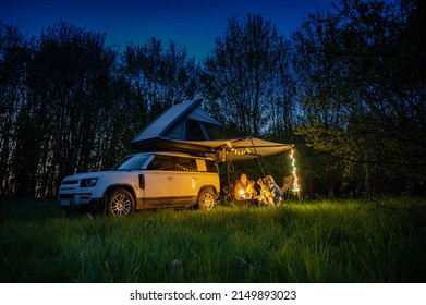 Man and woman with dogs camping in front of a 4x4 Offroad vehicle with roof tent at night time and romantic lighting
