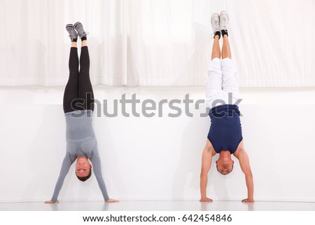 Man and woman doing handstand exercise in gym