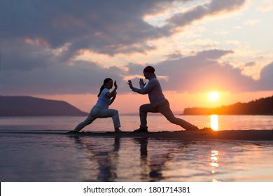 Man And Woman Doing Tai Chi Chuan At Sunset On The Beach.  Solo Outdoor Activities. Social Distancing. Healthy Lifestyle  Concept. 