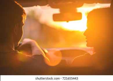 The man and woman drive a car on the background of the sunset
