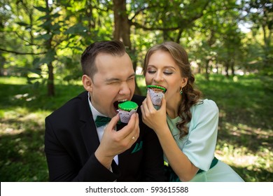 Man And Woman Eating Green Cupcakes In Park. Bride And Groom Having Fun On Green Wedding Or Saint Patrick Day