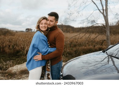 A man and a woman embrace happily in front of a car, smiling under the sky - Powered by Shutterstock