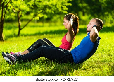 Man And Woman Exercising At The City Park. Beautiful Young Multiracial Couple. Sit Ups Fitness Couple Exercising Outside In Grass. Fit Happy People Working Out Outdoor.