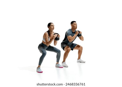 Man and woman exercising with kettlebells in squat position against white studio background. Athletic movements. Concept of people in sport, healthy lifestyle, teamwork, motivation. Ad - Powered by Shutterstock