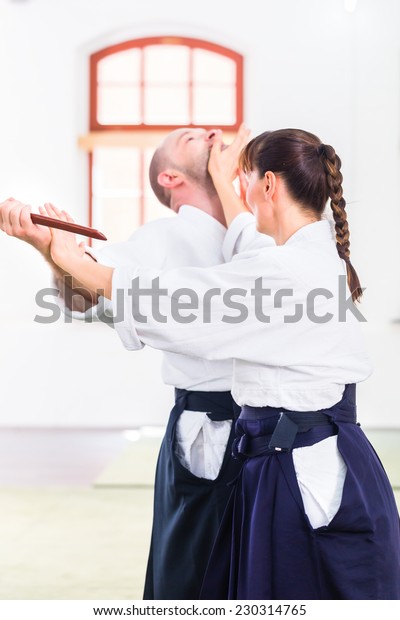 Man and woman fighting with wooden knifes at\
Aikido training in martial arts school\
