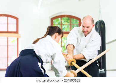 Man and woman fighting with wooden swords at Aikido training in martial arts school 
