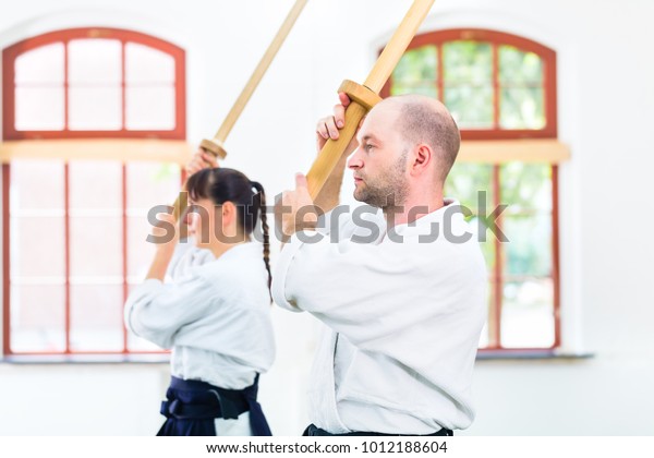 Man and woman fighting with wooden swords at\
Aikido training in martial arts school\

