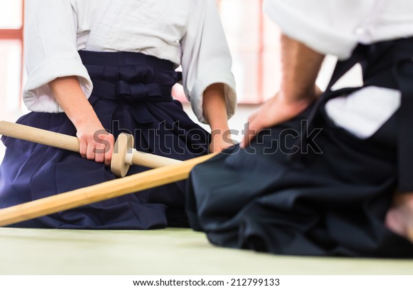 Man and woman fighting with wooden swords at\
Aikido training in martial arts school\
