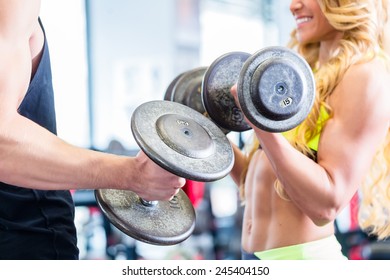 Man and woman in fitness gym lifting dumbbells looking at each other 