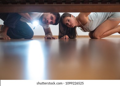 The Man And A Woman With A Flashlight Looking Under The Bed