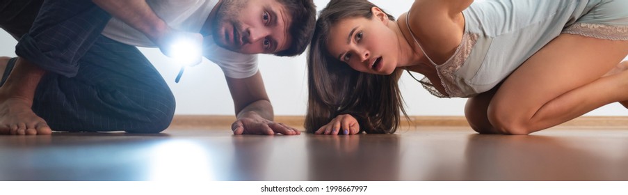 The Man And A Woman With A Flashlight Looking Under The Bed