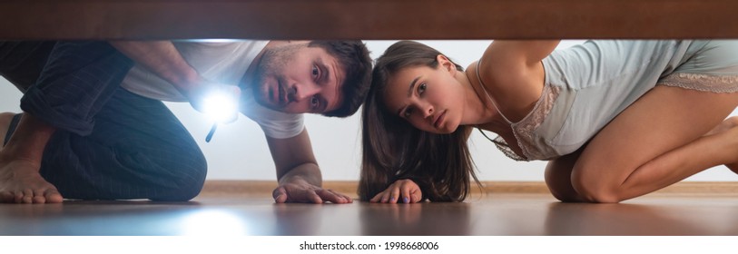 The Man And A Woman With A Flashlight Looking Under The Bed