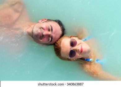 A Man And Woman Float In Blue Lagoon Spa Resort In Iceland, Their Heads Are In Front Each Other