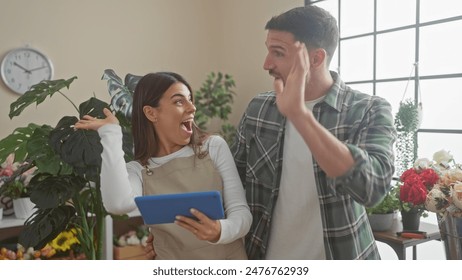 A man and woman, florists, high-five joyfully in a flower shop filled with green plants and colorful bouquets. - Powered by Shutterstock