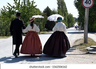 A man and a woman go hand in hand, in nineteenth-century clothing. A man in a frock coat, in a celindra and with a cane, a woman in a luxurious, long dress, in a hat and with an umbrella - Shutterstock ID 1562506162