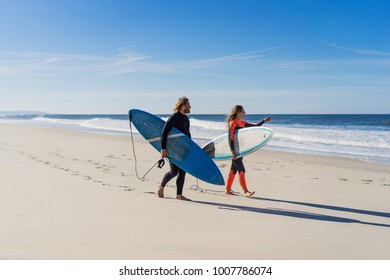 Man And Woman Go To The Ocean With Surf Boards. Man And Girl Go Surfing, Portugal, Nazare. Surfing In A Wet Suit.