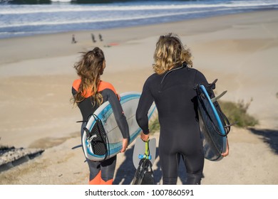 Man And Woman Go To The Ocean With Surf Boards. Man And Girl Go Surfing, Portugal, Nazare. Surfing In A Wet Suit.