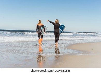 Man And Woman Go To The Ocean With Surf Boards. Man And Girl Go Surfing, Portugal, Nazare. Surfing In A Wet Suit.