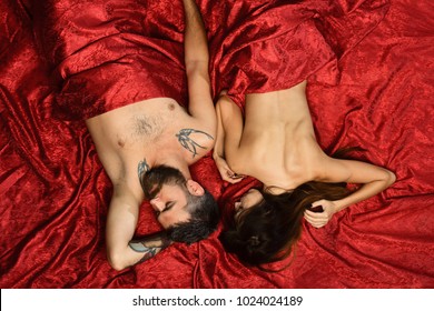 Man and woman with half covered bodies sleep in their bedroom. Love and sex concept. Couple in love on red sheets. Guy with beard lies close to pretty lady in bed, top view