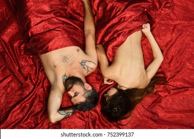 Man and woman with half covered bodies lie in bedroom. Guy with beard and calm face sleeps with pretty lady in bed, top view. Couple in love on red sheets. Love and sex concept.
